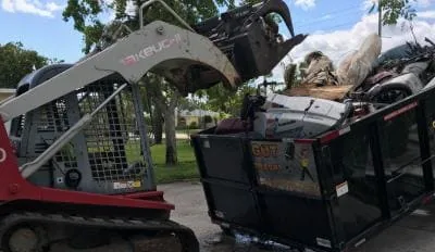 Bobcat equipment loading debris into dumpster for junk removal in South Florida